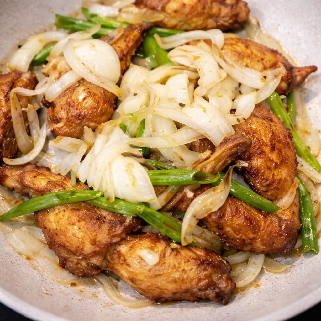 Fried chicken wings tossed with sliced onions and spring onions in a pan