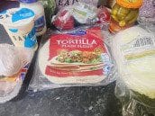 A pack of plain flour tortillas placed on a kitchen counter, surrounded by other shawarma ingredients like mayonnaise, pickles, and lettuce.