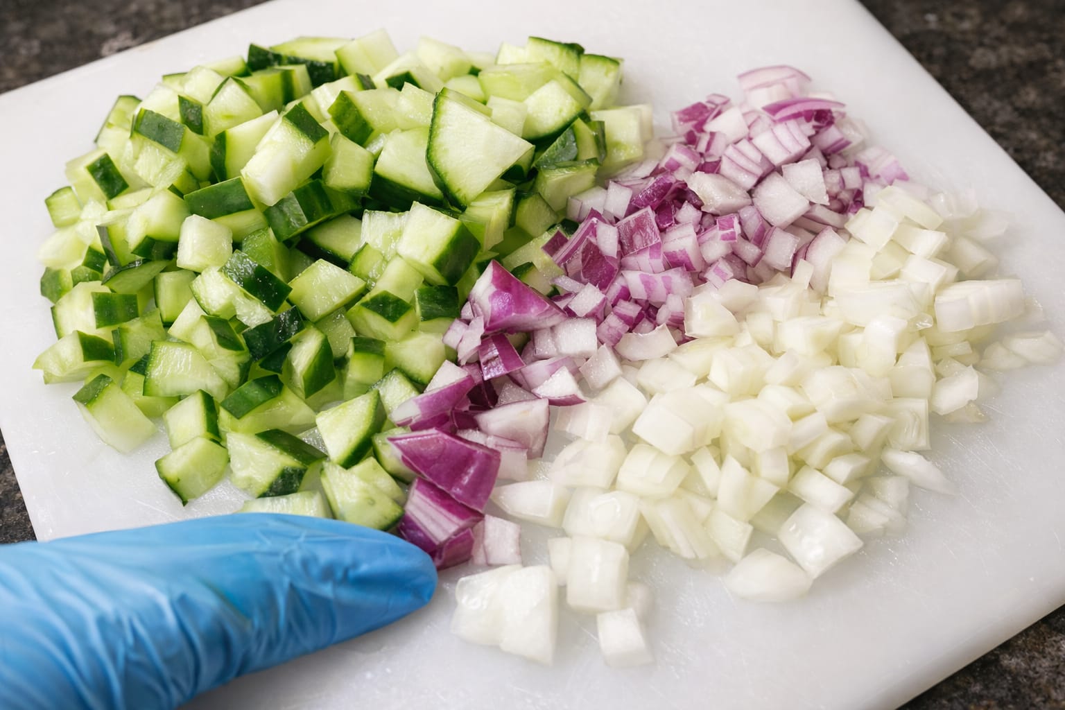 Chopped cucumber, red onion and white onion on a cutting board ready for avocado toast topping