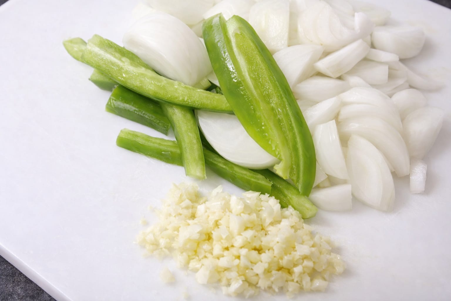 Chopped onion, green pepper slices, and minced garlic prepared on a cutting board for cooking