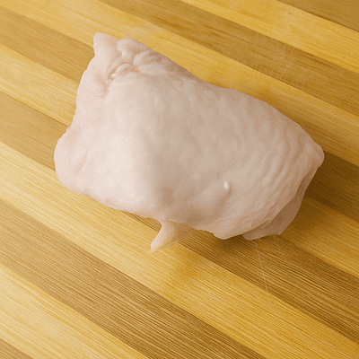 Deboning a raw chicken thigh on a wooden board