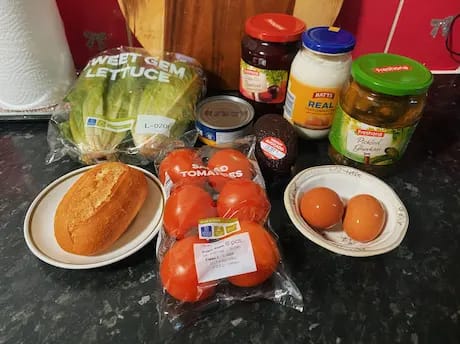 Ingredients laid out for homemade breakfast plate with eggs, avocado, salad, and bread