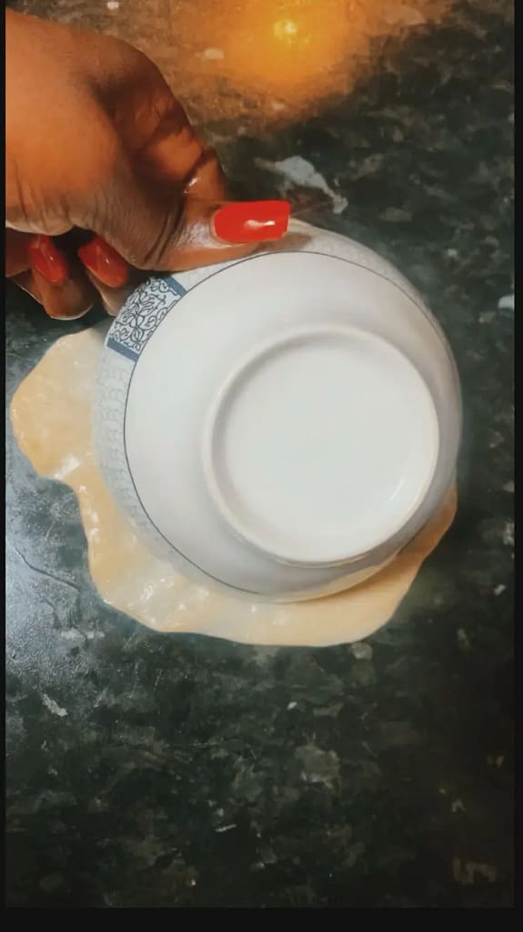 A person shaping naan dough on a countertop using a bowl to flatten it into a round shape.