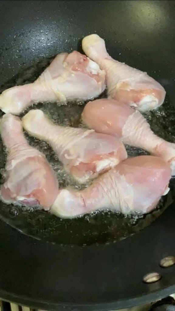 Chicken drumsticks frying in oil until golden brown in a deep saucepan.