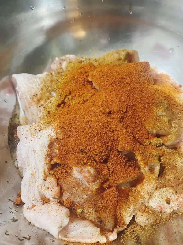 Raw chicken thighs in a mixing bowl topped with paprika, garlic, and seasoning, ready for marination.