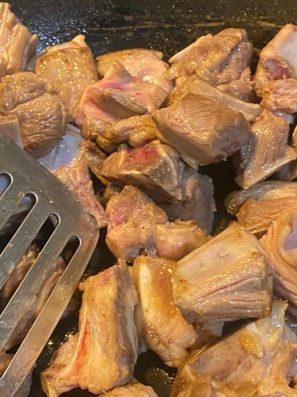Close-up of meat pieces searing in a hot pan until golden brown.