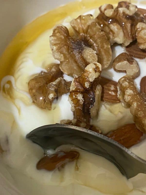 Bowl of yogurt topped with almonds, walnuts, and honey drizzle.