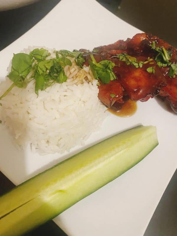 Plated BBQ chicken with white rice, herbs, and cucumber slice on a white dish