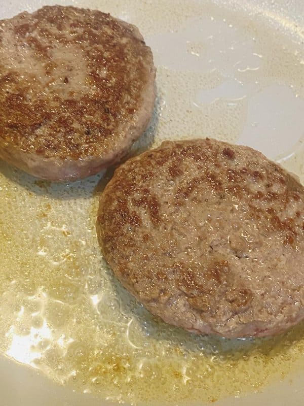 Juicy beef burger patties sizzling in a frying pan.