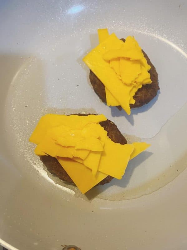 Beef patties topped with melting cheese slices in a frying pan.