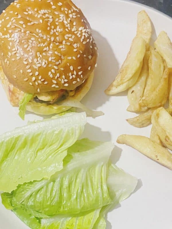 Gourmet beef burger with sesame seed bun, crispy fries, and fresh lettuce on a white plate.