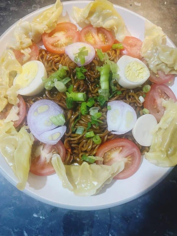 A full plate of Vegetable Dumplings with Noodles garnished with eggs, tomatoes, onions, dumplings, and fresh spring onions.