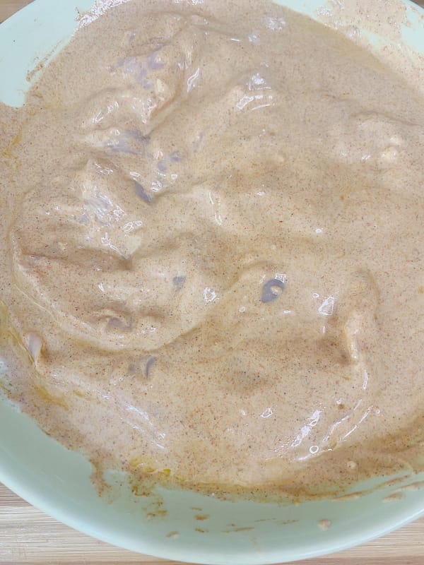 Raw chicken pieces coated in creamy yogurt-based marinade on a tray.