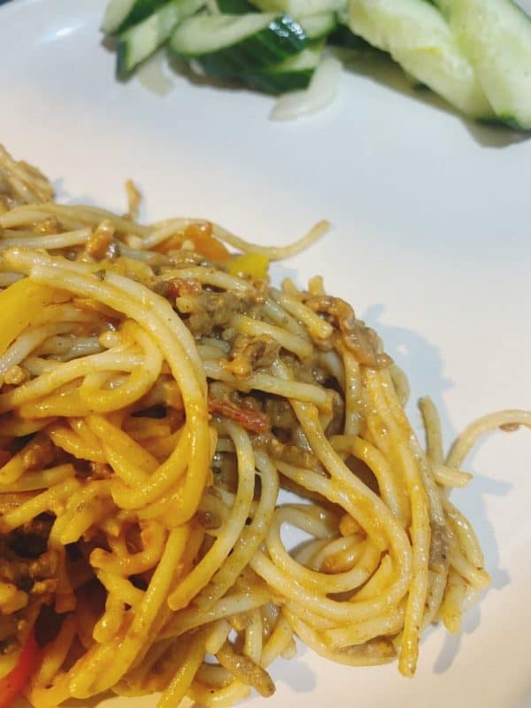 Creamy spaghetti with minced beef served on a white plate, accompanied by a fresh cucumber and onion salad.