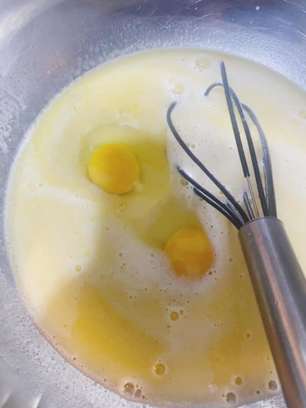 Two eggs in a bowl of liquid mixture with a whisk.