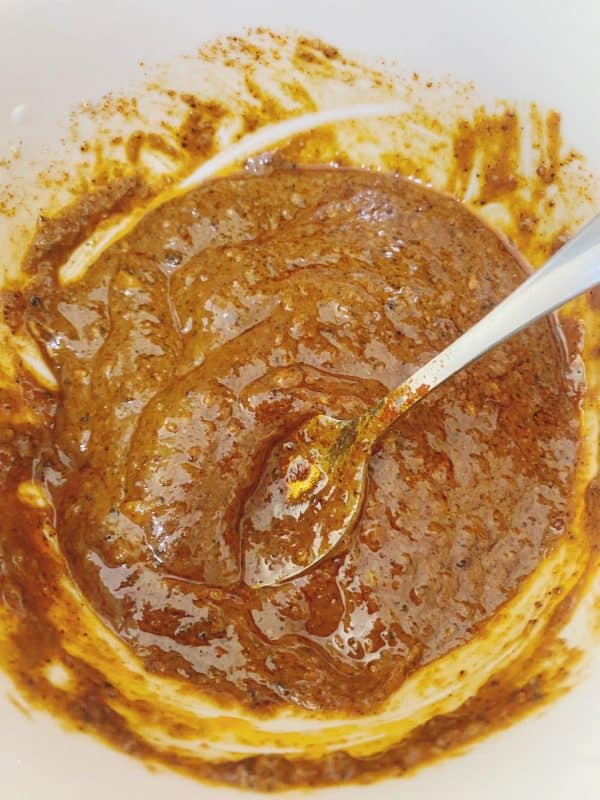 Thick and glossy brown marinade is fully mixed in a white bowl with a spoon