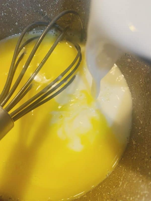 Milk being poured into melted butter with a whisk.