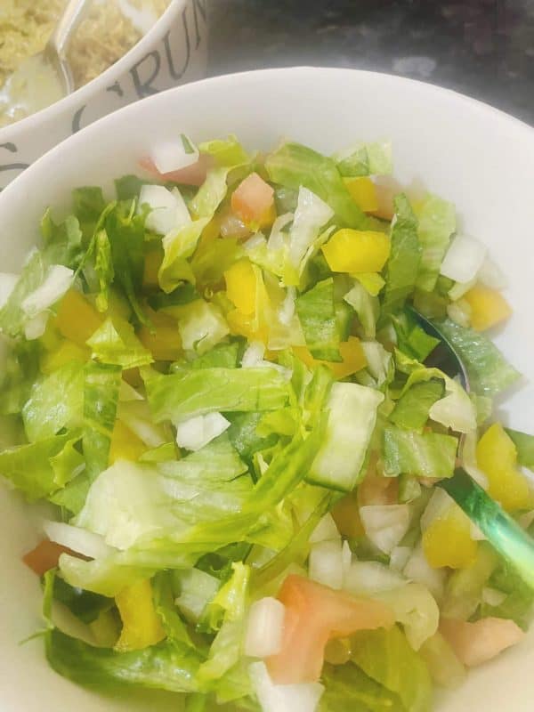 Chopped onion, cucumber, lettuce, and tomato being added to the mashed mackerel in a mixing bowl.