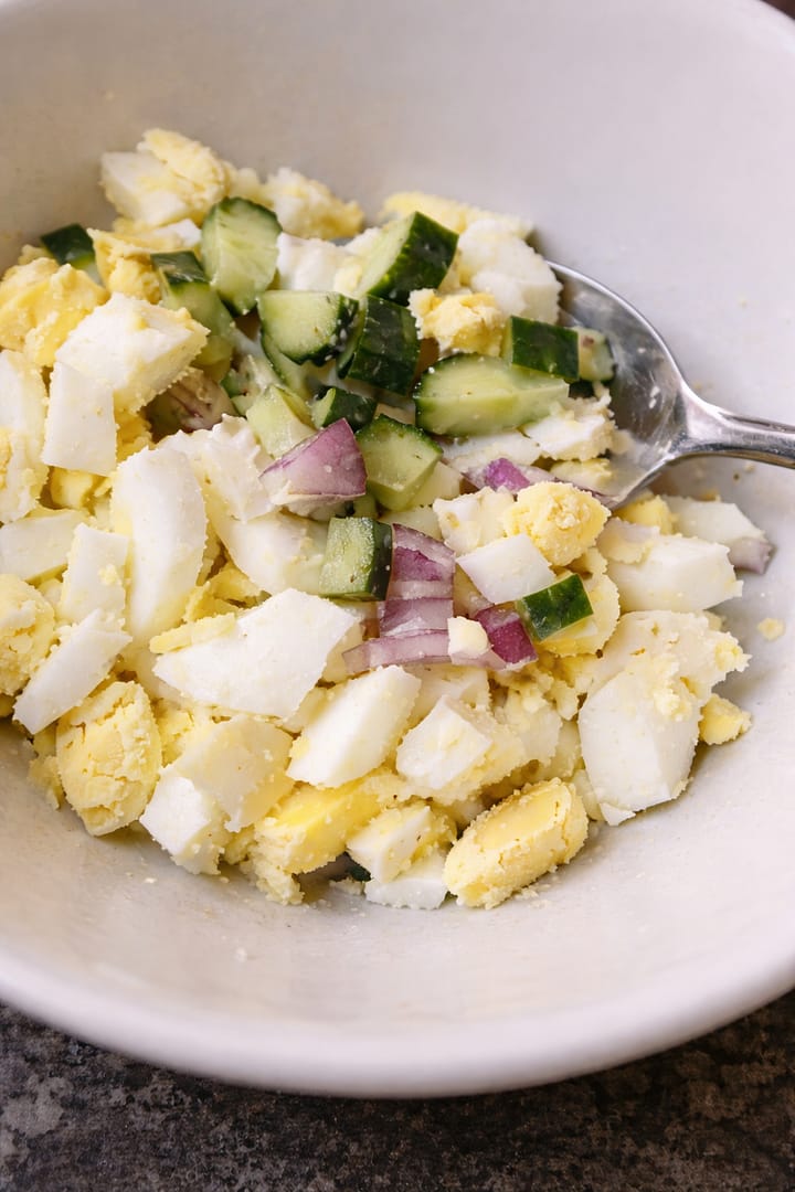 Chopped boiled eggs mixed with cucumber and red onion in a bowl for avocado egg toast topping
