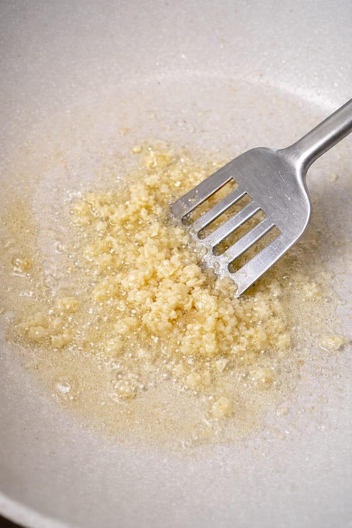 Minced garlic frying in oil in a pan while being stirred with a spatula