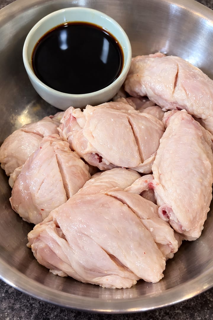 Raw chicken wings in a mixing bowl with seasoning and soy sauce ready for marinating