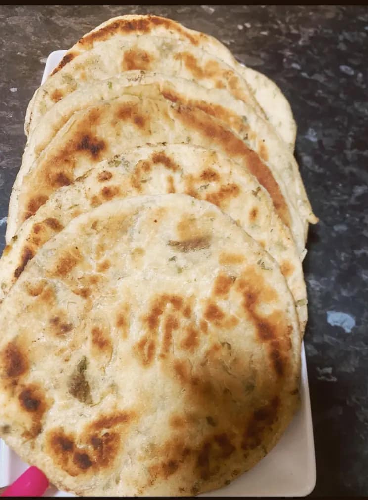 A stack of freshly cooked golden-brown parsley naan breads arranged neatly on a white plate.