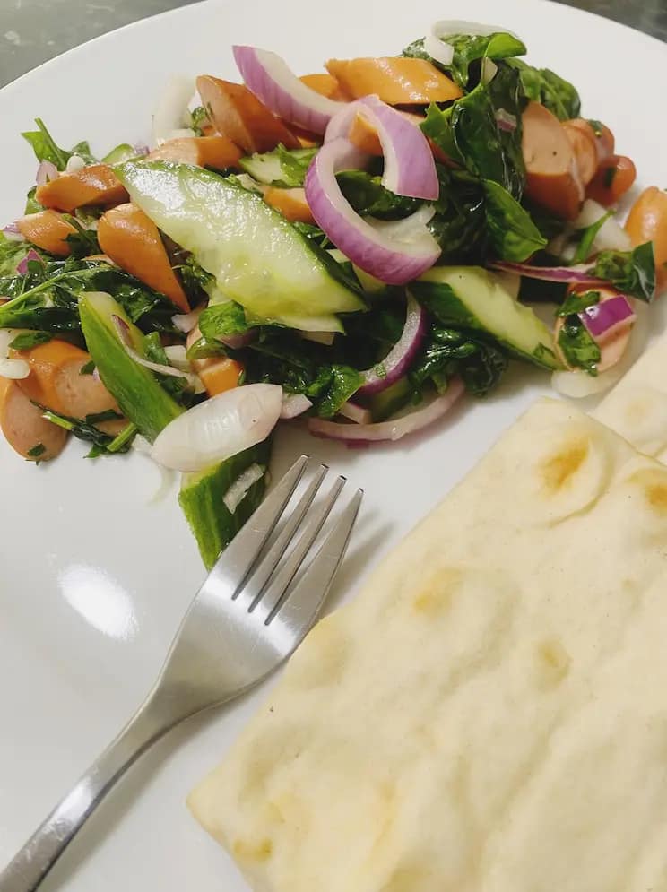 Spinach and sausage salad served with naan bread on a white plate.