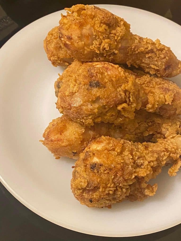 Golden crispy fried chicken drumsticks on a white plate.