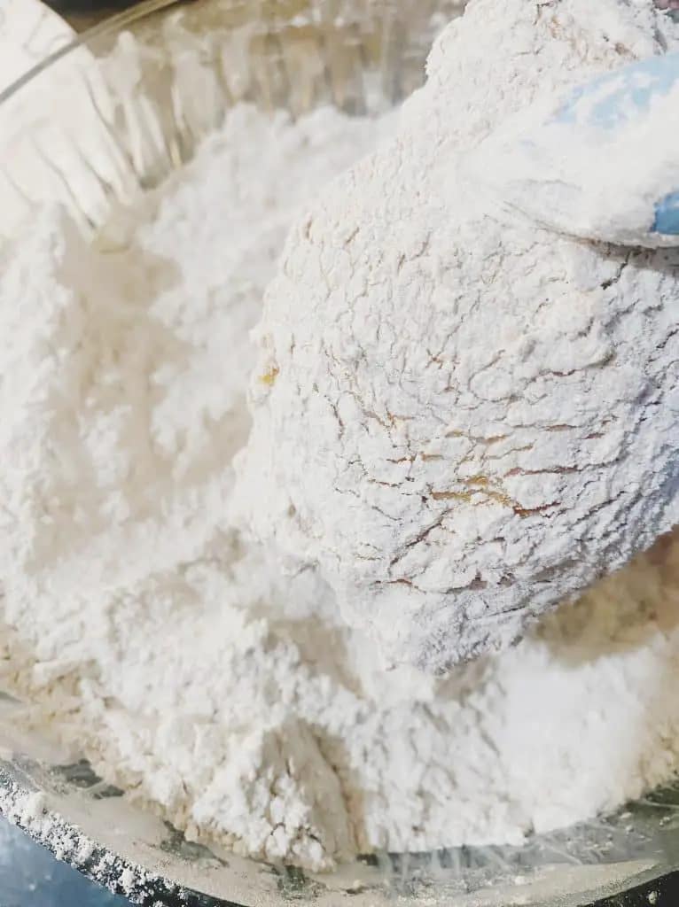 Chicken thigh coated in seasoned flour for frying.