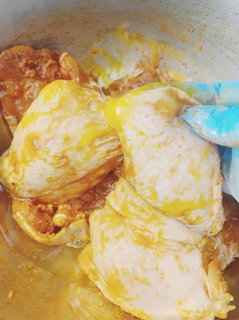 Marinated chicken thighs being dipped into whisked egg wash for coating.