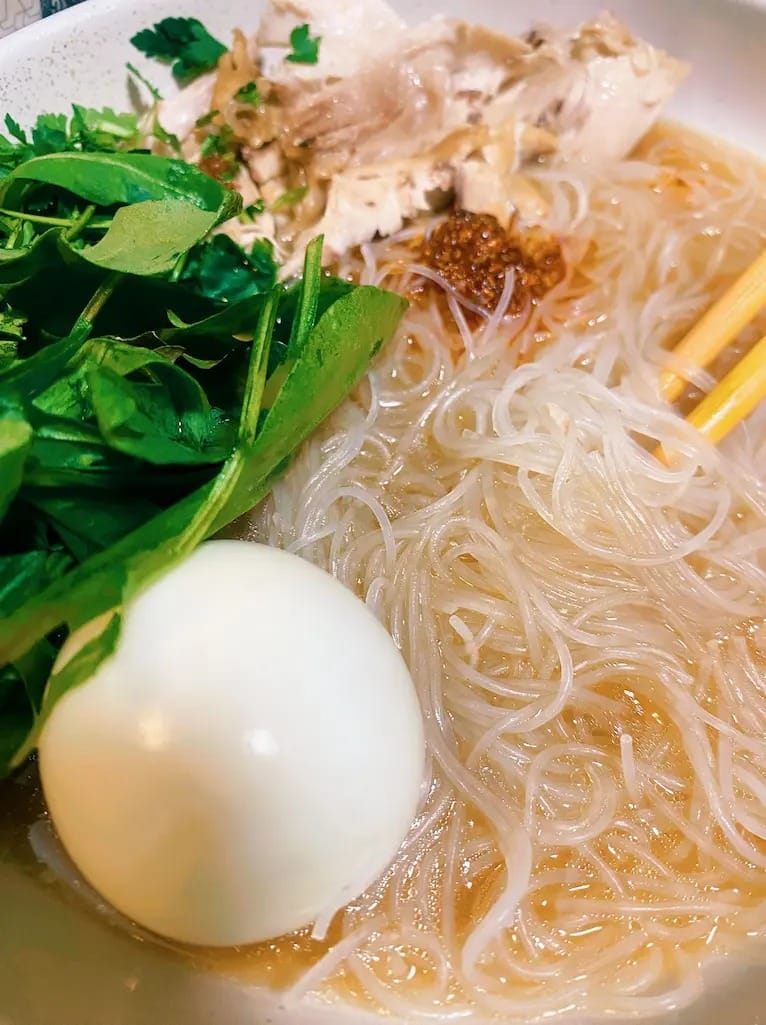 Rice noodle soup with chicken, boiled egg, fresh herbs, and chili paste