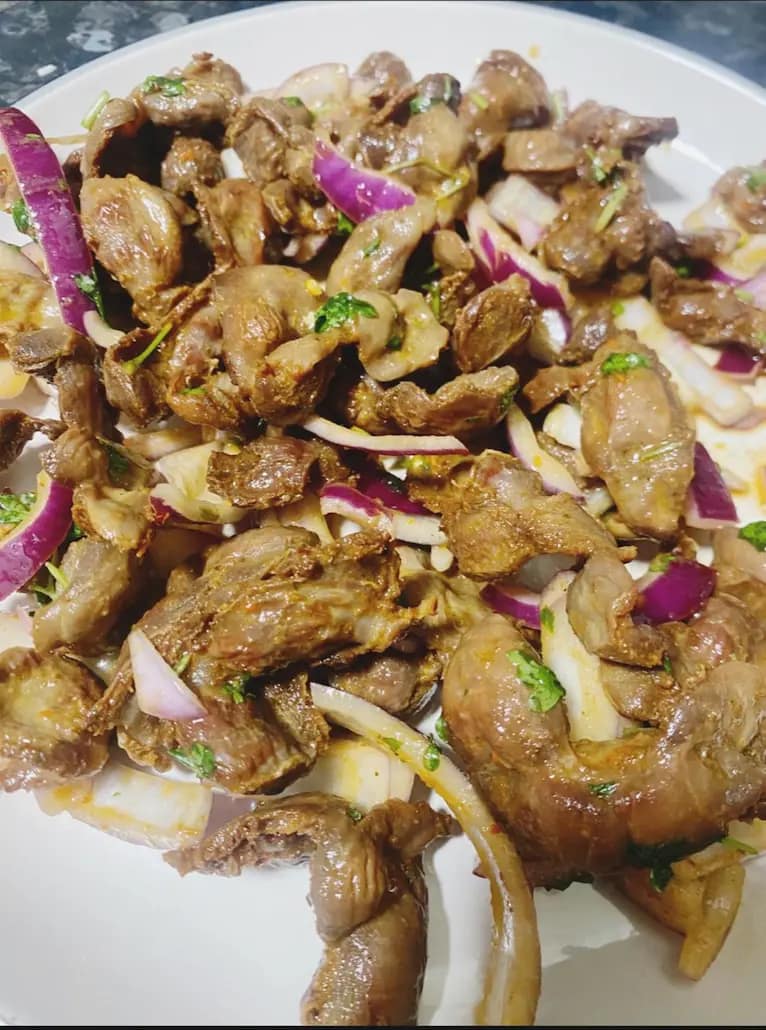 Plated chicken gizzards mixed with red onion slices and parsley, ready to be served