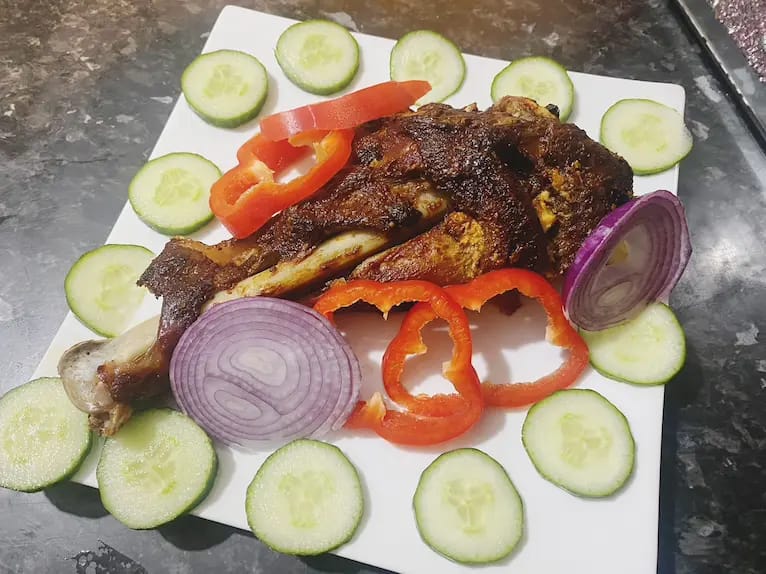 Roasted turkey leg served with cucumber, red paprika, and onion slices.