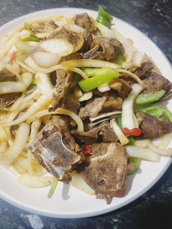 Roasted lamb pieces topped with fresh onions and peppers, ready to serve.