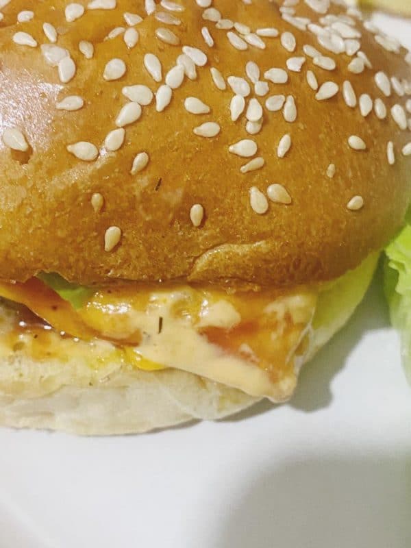 Close-up of a homemade cheeseburger with sesame seed bun, sauce, tomato, lettuce, and melted cheese.