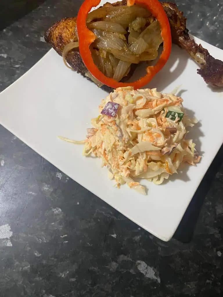Fried chicken leg with caramelized onions and red pepper, served with cabbage and carrot salad.