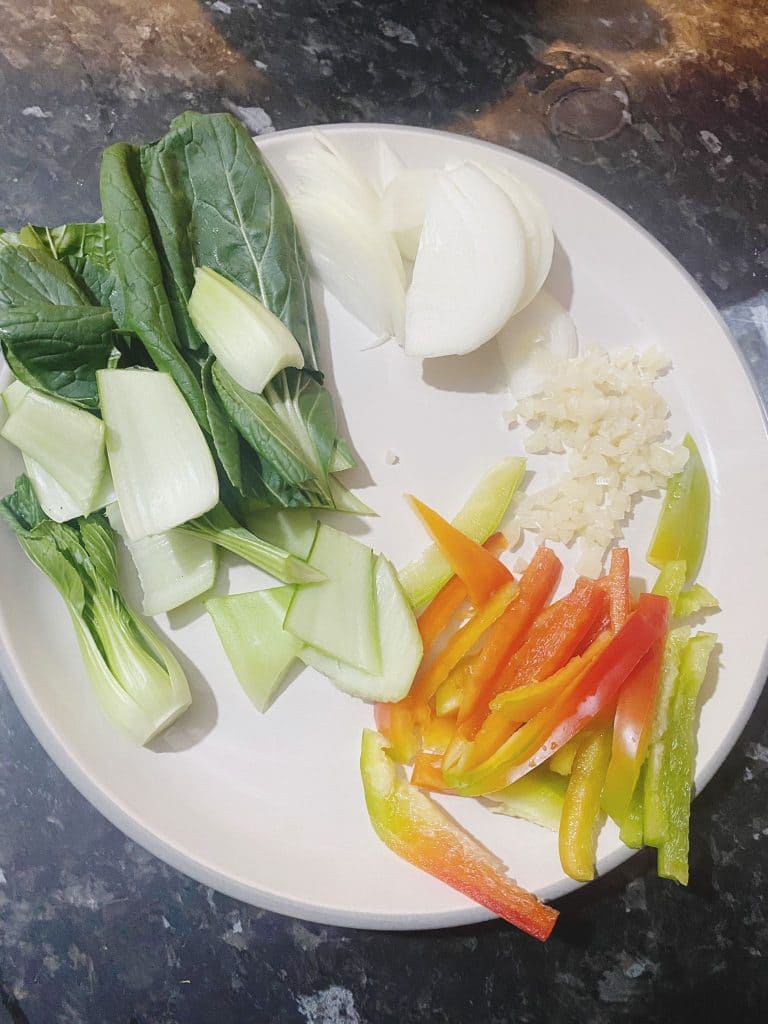 Freshly chopped vegetables for chicken stir-fry including pak choi, onion, bell peppers, and garlic.