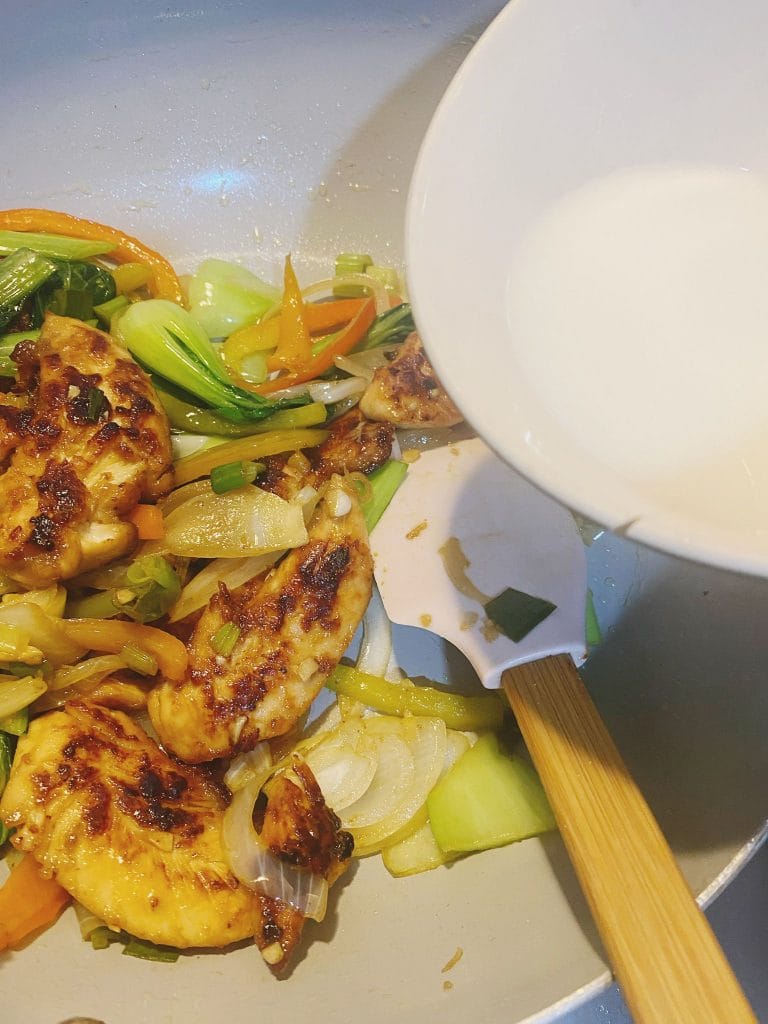 Stir-fried chicken and vegetables in a pan with a cornflour slurry being added to thicken the sauce.