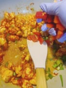 Chopped green onions and red bell peppers being added to a pan of seasoned chicken.