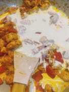 Cream being poured into a pan of tomato-coated chicken and vegetables.