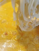 Cooked pasta being added to a creamy cheese sauce in a pan.