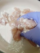 Chicken pieces in a bowl coated with cornflour, salt, and crumbled Oxo cube, ready for frying