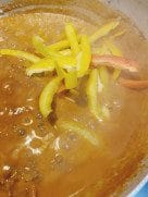 Creamy beef and tomato sauce simmering in a pot with yellow and red bell pepper strips added on top.