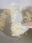 Diced onions being sautéed in oil inside a large pot with a wooden spatula.