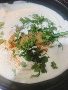 A bowl of thick yogurt topped with ground spices and fresh basil leaves before mixing.