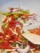 Colorful sliced onions and bell peppers sautéing in a skillet with a light oil sheen.