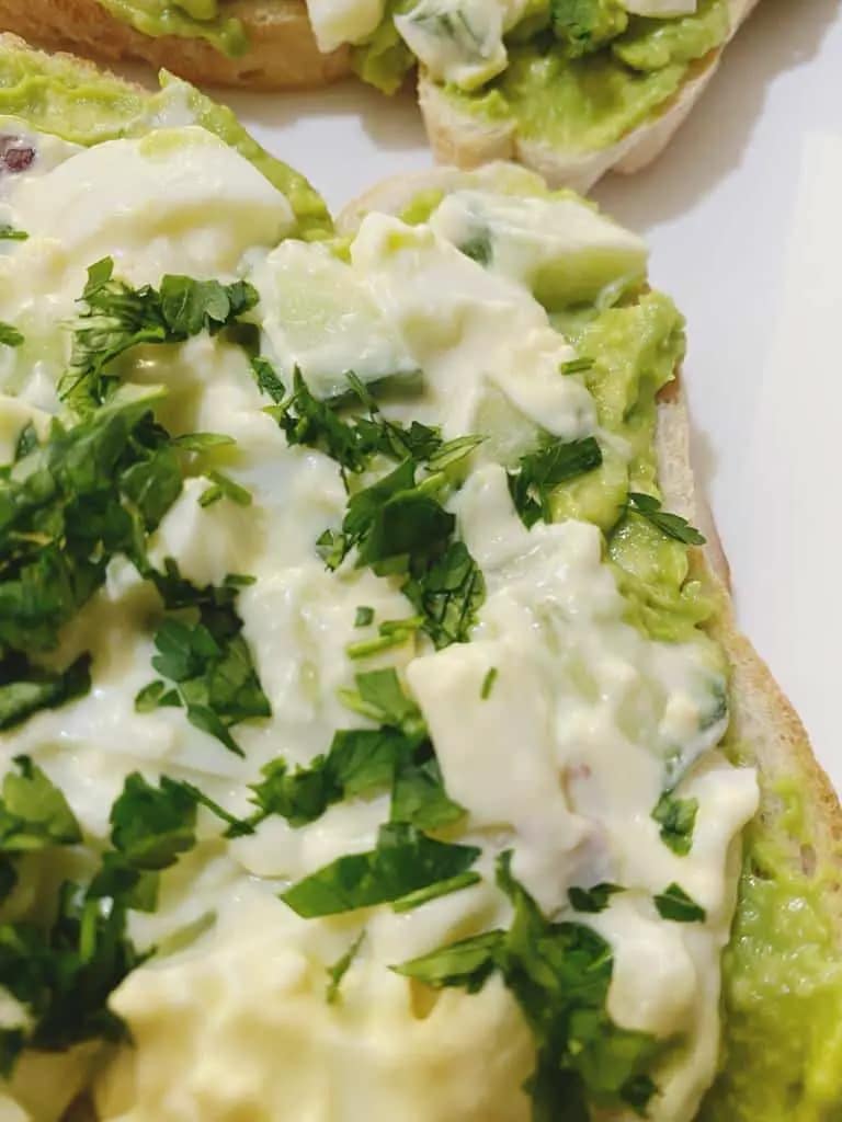 Avocado toast topped with creamy egg mixture and fresh chopped parsley