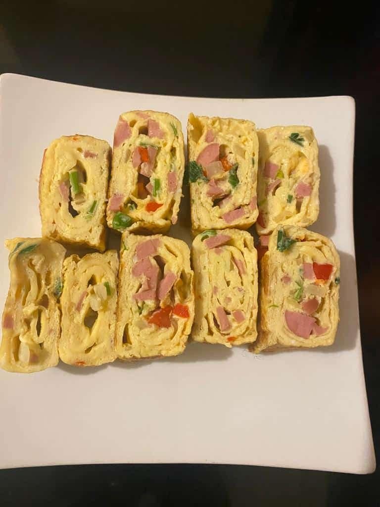 Rolled omelet slices fanned out on a plate, garnished with green onions and served with a small salad and dipping sauce