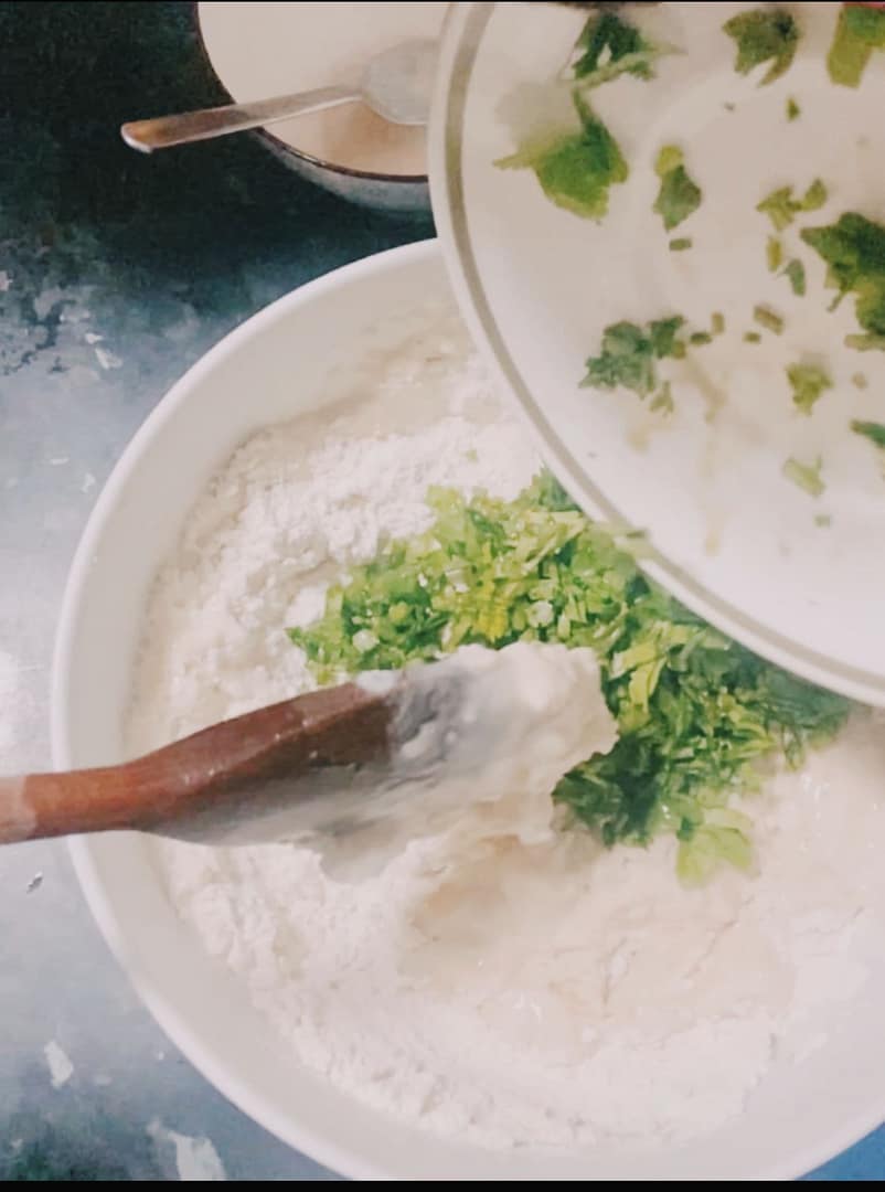 Fresh parsley being added to flour and yeast mixture for soft parsley naan dough