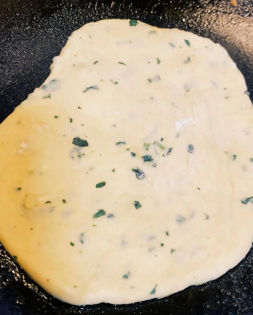 Fresh parsley naan cooking in a pan, beginning to turn golden on the edges.